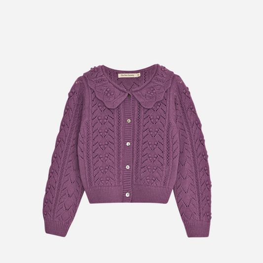 Sold at Bombon shop, this girls’ cardigan by The New Society features a rich lilac hue with an intricate pointelle knit pattern, scalloped Peter Pan collar, and front button closure—offering a refined and feminine layer for cooler days. front