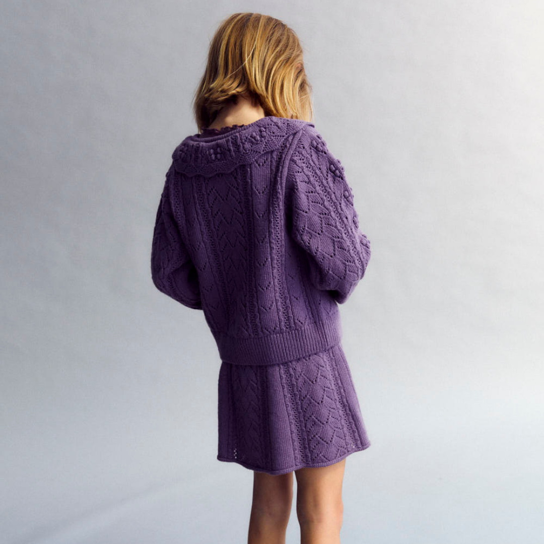 Sold at Bombon shop, this girls’ cardigan by The New Society features a rich lilac hue with an intricate pointelle knit pattern, scalloped Peter Pan collar, and front button closure—offering a refined and feminine layer for cooler days. model