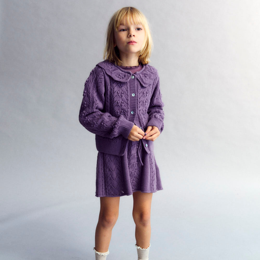 Sold at Bombon shop, this girls’ cardigan by The New Society features a rich lilac hue with an intricate pointelle knit pattern, scalloped Peter Pan collar, and front button closure—offering a refined and feminine layer for cooler days. model