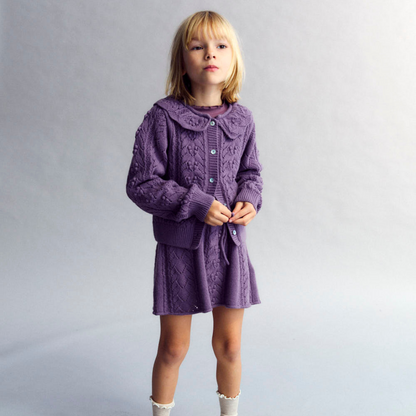 Sold at Bombon shop, this girls’ cardigan by The New Society features a rich lilac hue with an intricate pointelle knit pattern, scalloped Peter Pan collar, and front button closure—offering a refined and feminine layer for cooler days. model