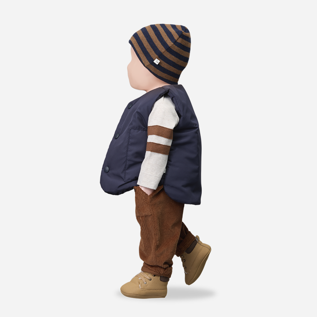 Child wearing a navy jacket, striped hat, and brown pants on a white background