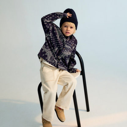 Sold at Bombon shop, this baby and toddler boy shirt by The New Society features a bold navy and white bandana-style print, long sleeves, front buttons, and a chest pocket embroidered with “TNS” for a stylish, laid-back look. model version