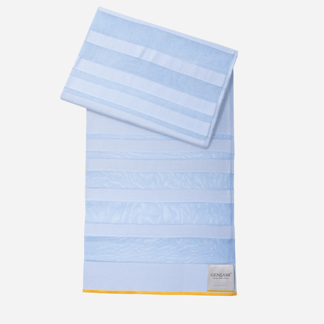 Sold at Bombon and designed by Gensami, a blue newborn layette set including a knit jumpsuit, hat, socks, and matching blanket with yellow stripe detailing.