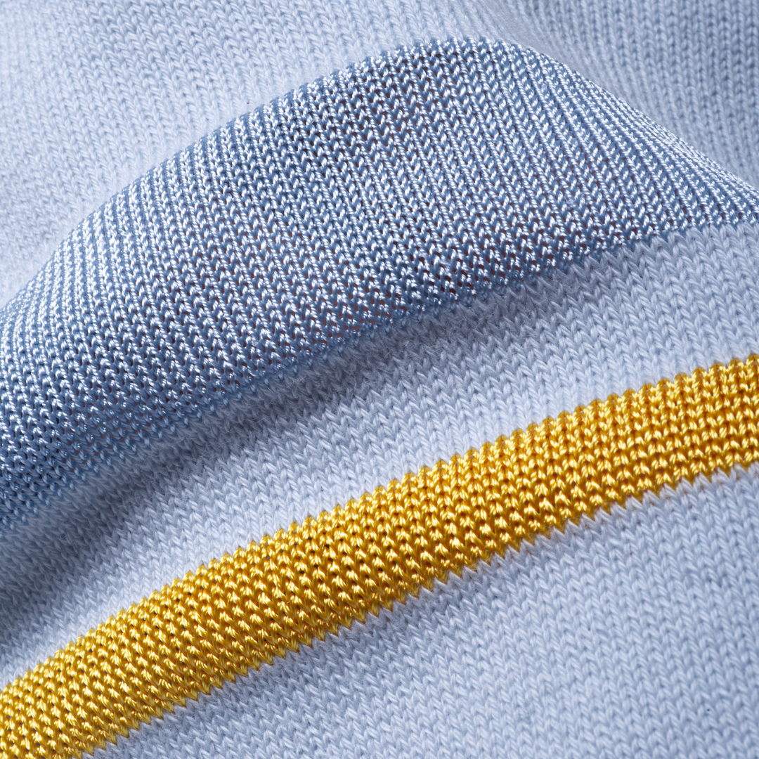 Sold at Bombon and designed by Gensami, a blue newborn layette set including a knit jumpsuit, hat, socks, and matching blanket with yellow stripe detailing.