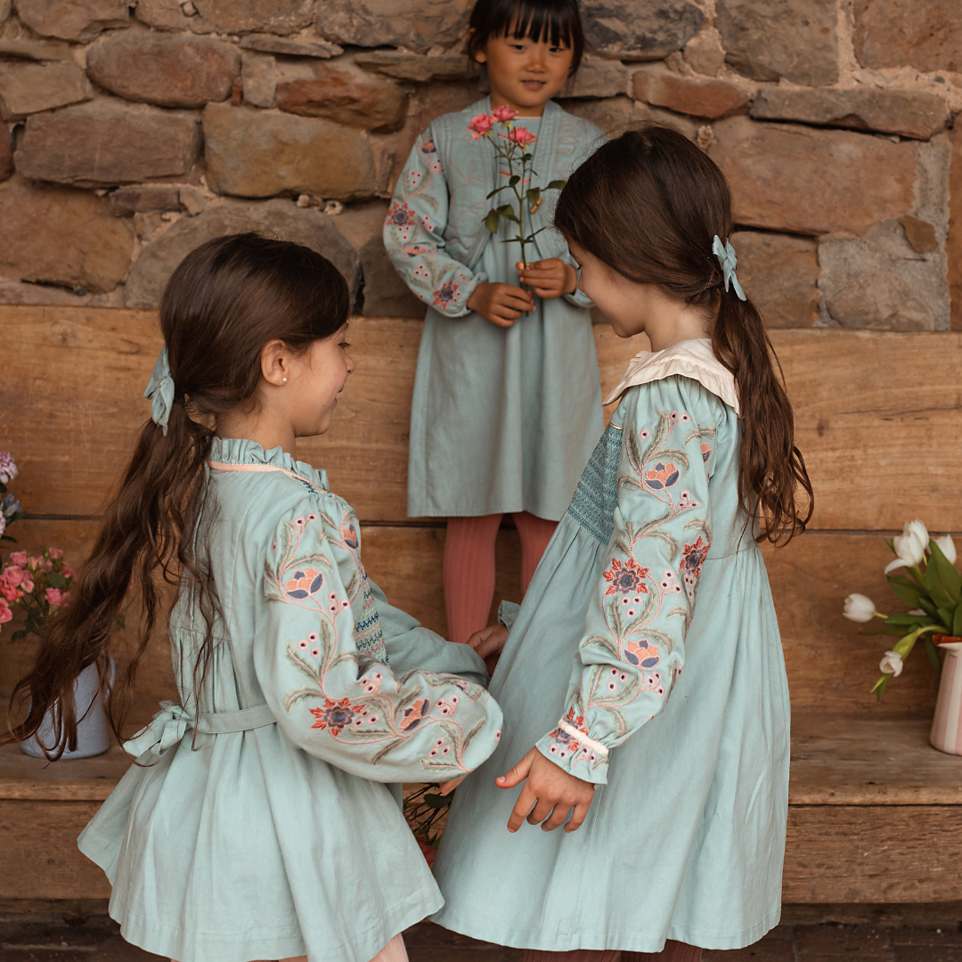 sold at Bombon shop, designed by Bachaa, Blouse/Short dress, Blue color, Organic cotton twill (167 g/m²), Plain lining in organic cotton voile, Long embroidered and elasticated sleeves, Smocked chest, Ruffled collar, Tone-on-tone buttons and belt at the back. Model view