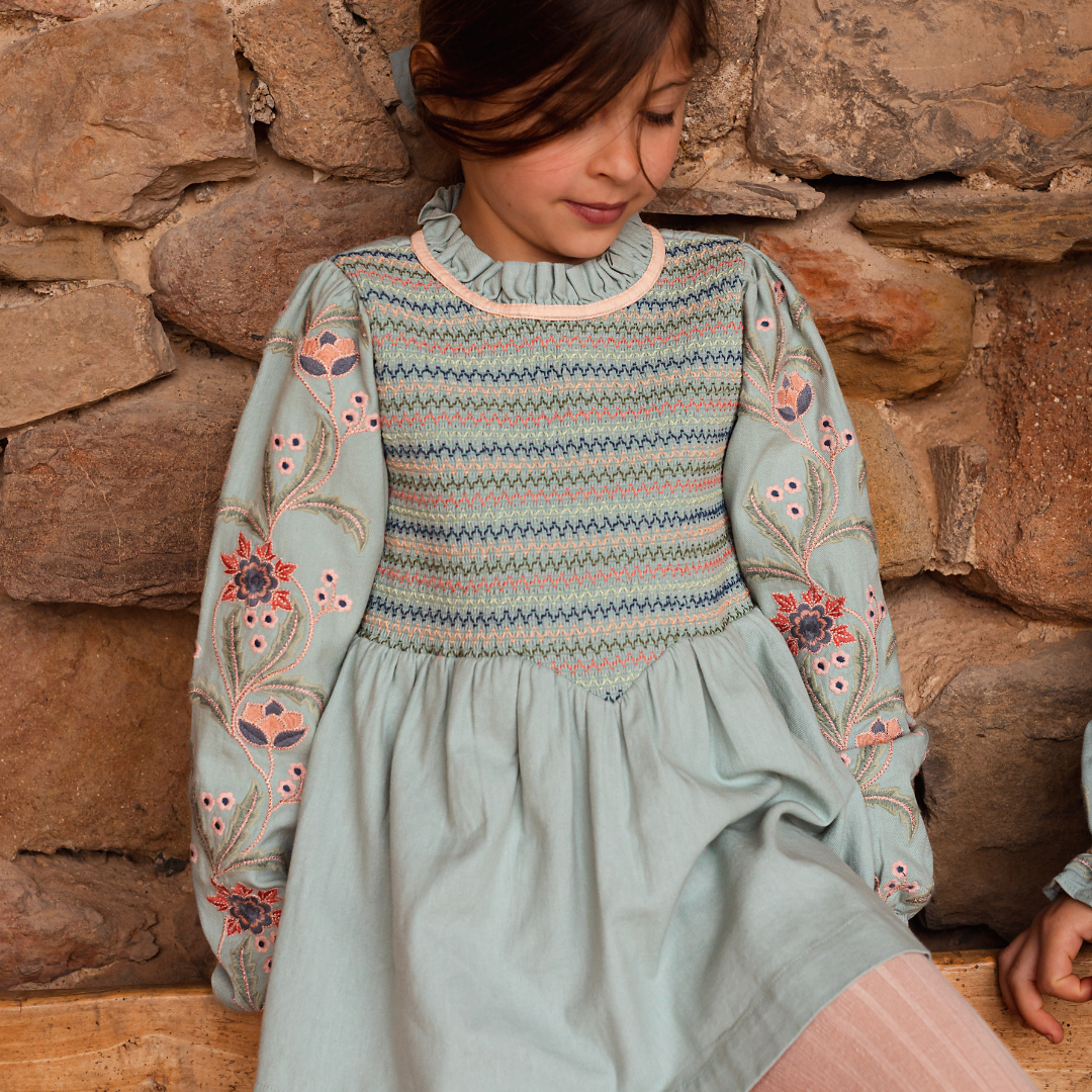 sold at Bombon shop, designed by Bachaa, Blouse/Short dress, Blue color, Organic cotton twill (167 g/m²), Plain lining in organic cotton voile, Long embroidered and elasticated sleeves, Smocked chest, Ruffled collar, Tone-on-tone buttons and belt at the back. Model view