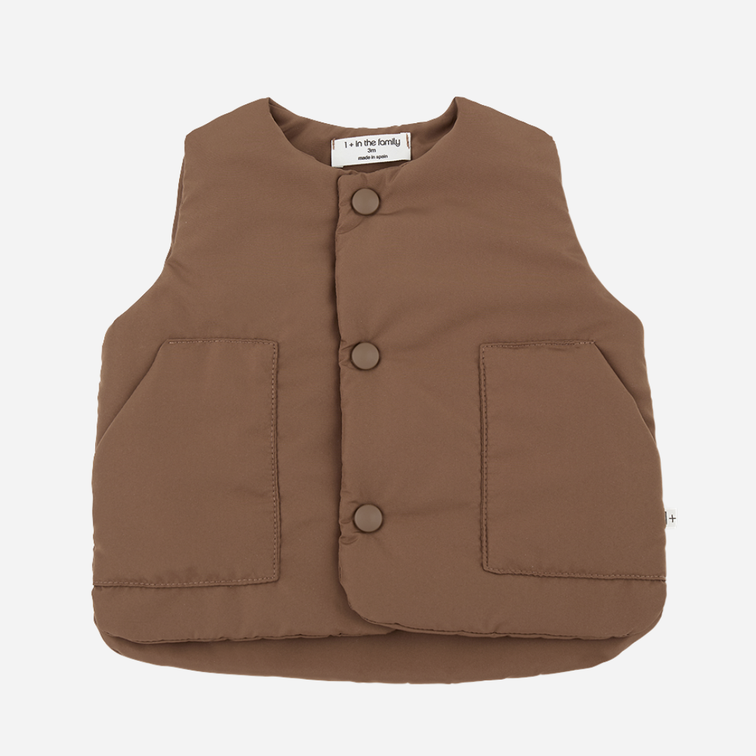 Sold at Bombon shop, designed by 1+ in the family — brown padded baby vest with front patch pockets and snap-button closure, laid flat on a white background.