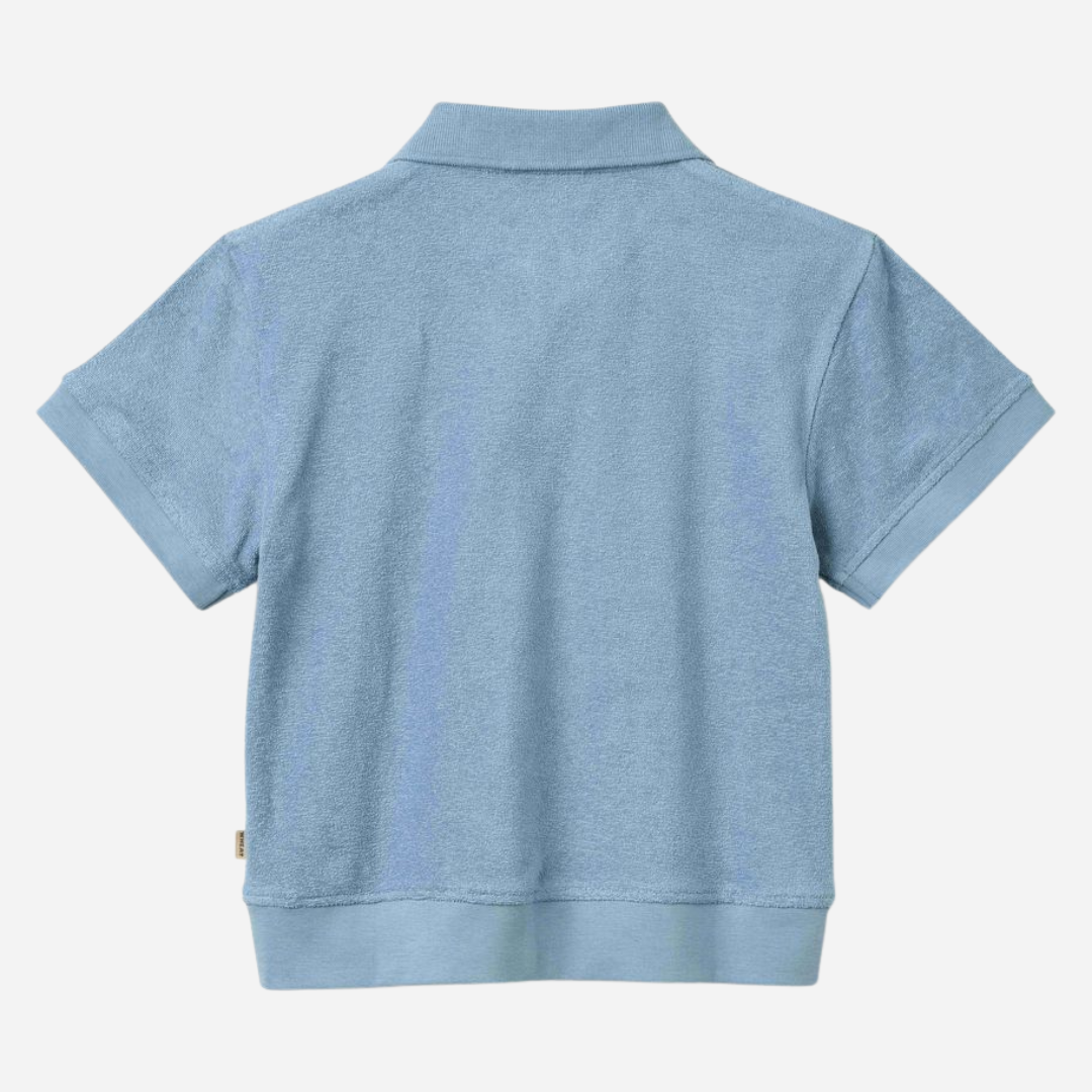 Sold at Bombon Shop, designed by Wheat, faded denim organic cotton short sleeve polo shirt with classic collar and soft blue washed tone.