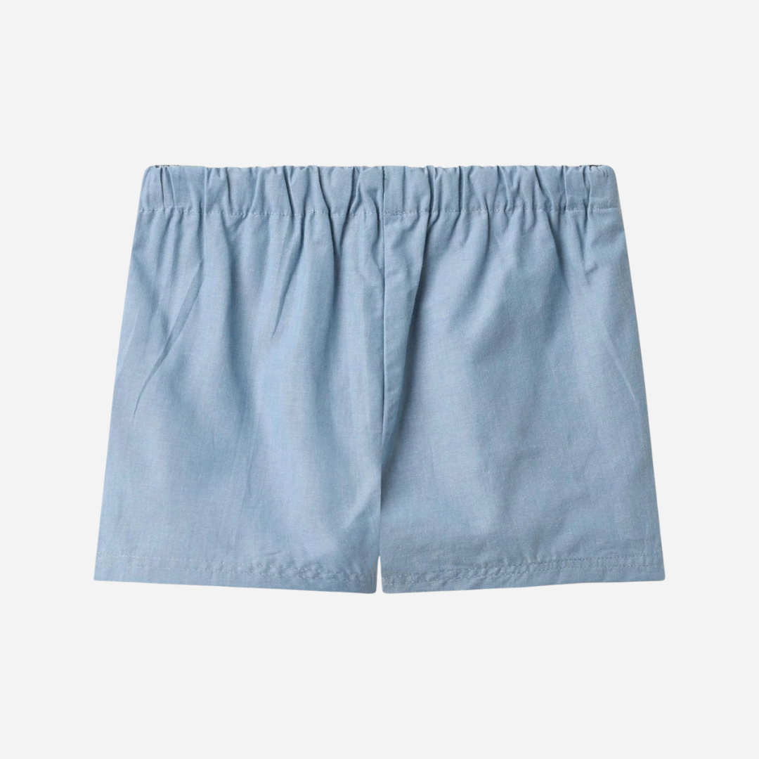 Sold at Bombon Shop, designed by Wheat, blue chambray organic cotton kids shorts with elastic waistband and drawstring detail.