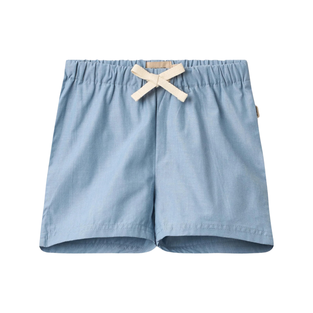 Sold at Bombon Shop, designed by Wheat, blue chambray organic cotton kids shorts with elastic waistband and drawstring detail.