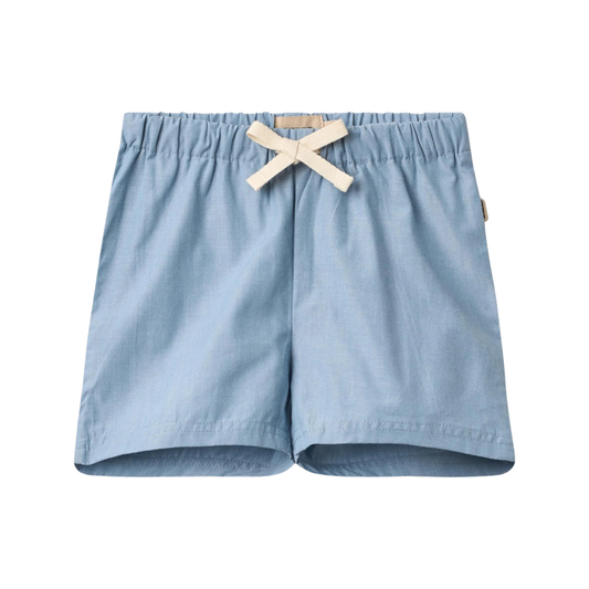 Sold at Bombon Shop, designed by Wheat, blue chambray organic cotton kids shorts with elastic waistband and drawstring detail.
