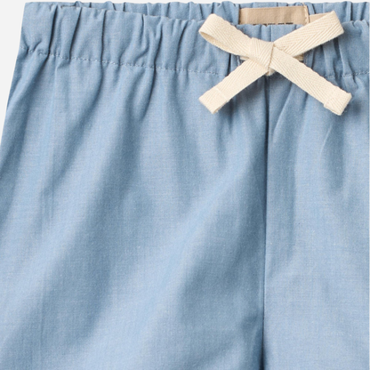 Sold at Bombon Shop, designed by Wheat, blue chambray organic cotton kids shorts with elastic waistband and drawstring detail.