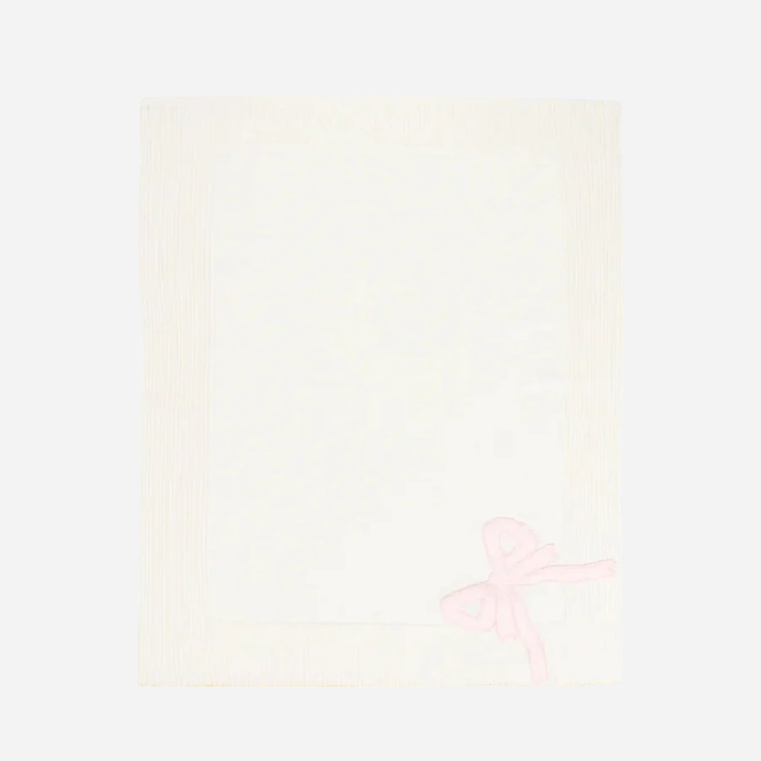 Sold at Bombon and designed by Gensami, a white merino wool baby blanket featuring a pink satin bow in one corner and yellow trim along the edge.