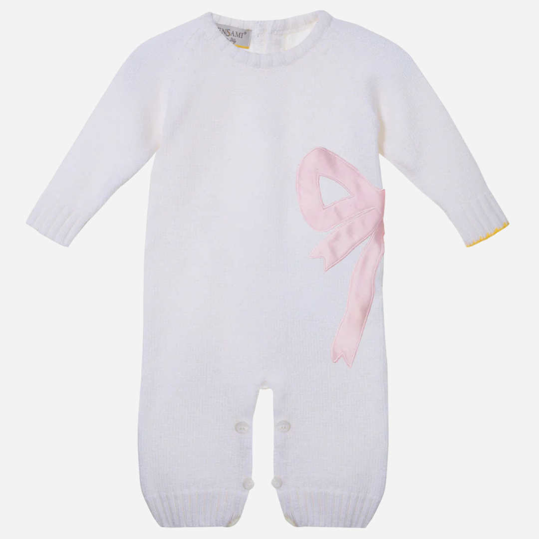 Sold at Bombon and designed by Gensami, a white merino wool baby romper with a pink satin bow on the side and yellow trim detail at the cuff.