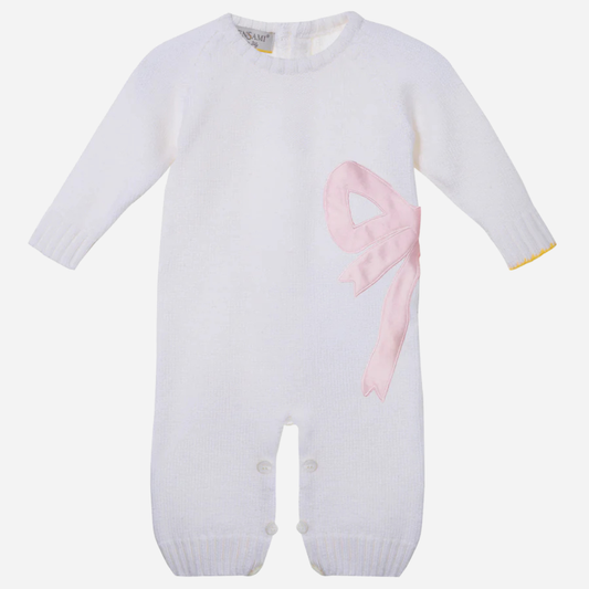 Sold at Bombon and designed by Gensami, a white merino wool baby romper with a pink satin bow on the side and yellow trim detail at the cuff.
