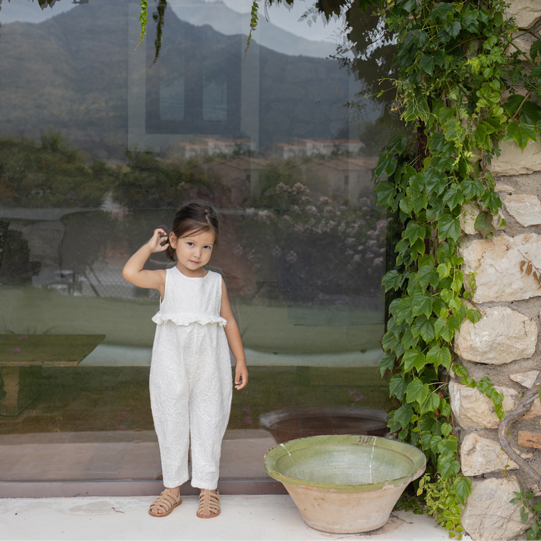 Sold at Bombon Shop, designed by 1+ in the family, off-white baby overall with textured cotton fabric and delicate ruffle detail across the chest.