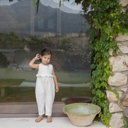 Sold at Bombon Shop, designed by 1+ in the family, off-white baby overall with textured cotton fabric and delicate ruffle detail across the chest.