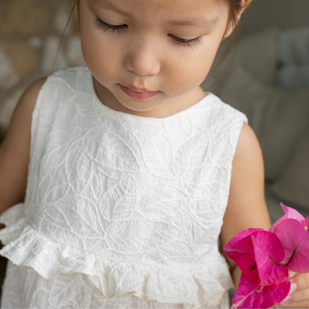 Sold at Bombon Shop, designed by 1+ in the family, off-white baby overall with textured cotton fabric and delicate ruffle detail across the chest.