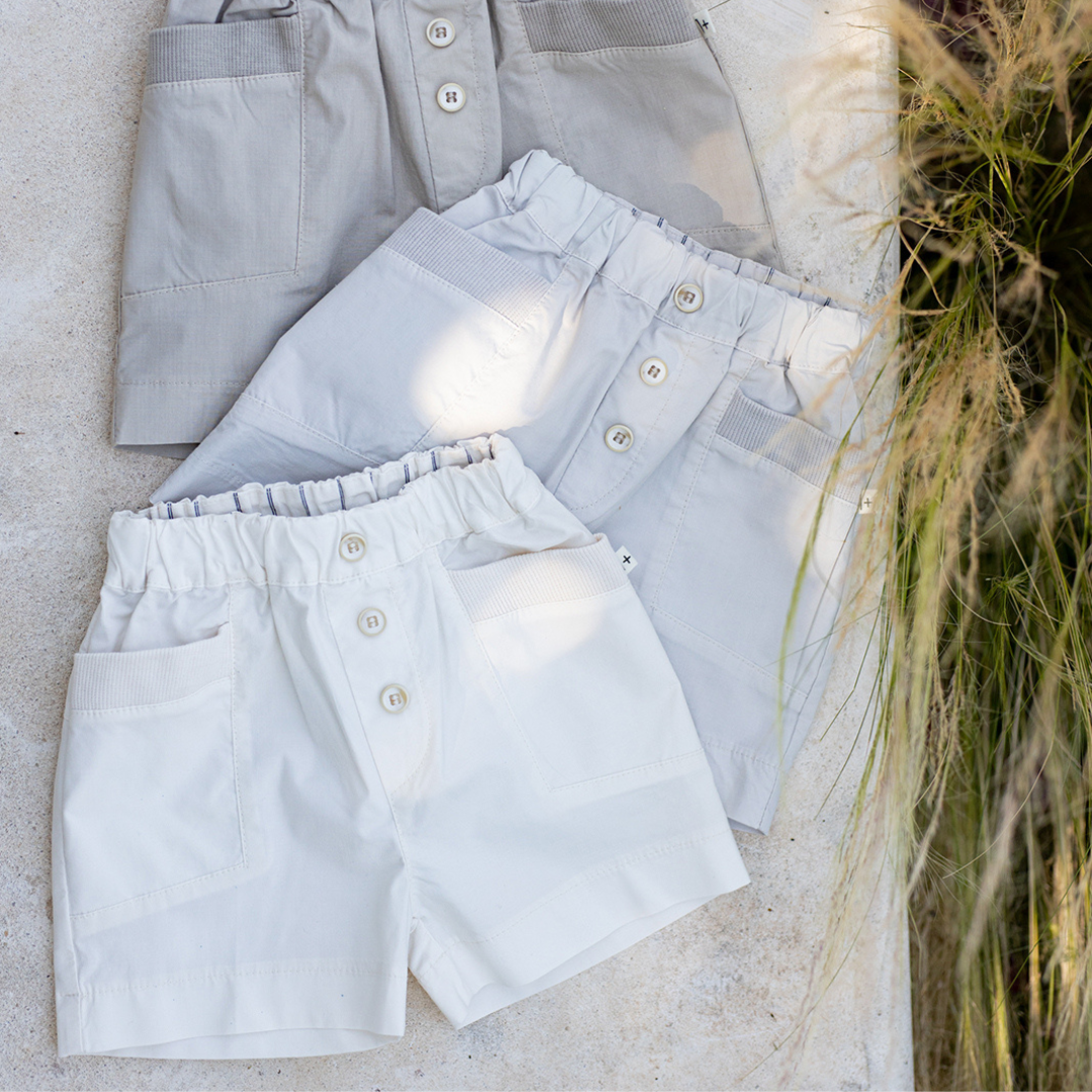 Sold at Bombon Shop, designed by 1+ in the family, off-white baby bermuda shorts with front button detail and soft cotton fabric.