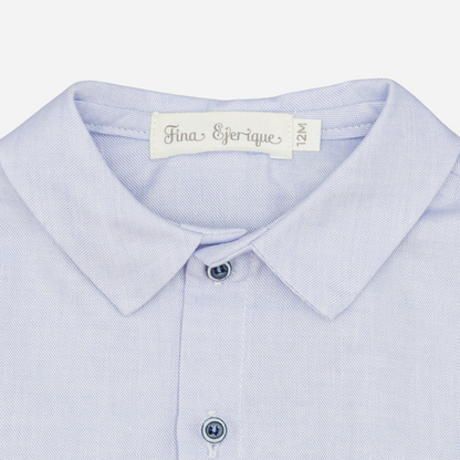 Sold at Bombon shop, designed by Fina Ejerique, a light-blue cotton baby shirt with rounded collar, long sleeves, and matching buttons. zoom