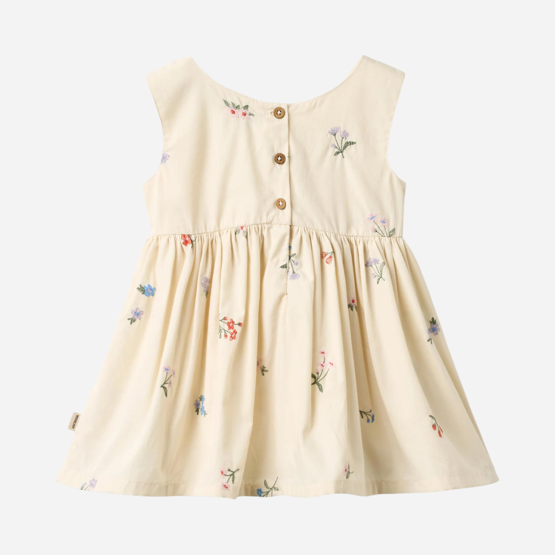 Sold at Bombon Shop, designed by Wheat, ivory organic cotton pinafore dress with embroidered floral details and gathered skirt.