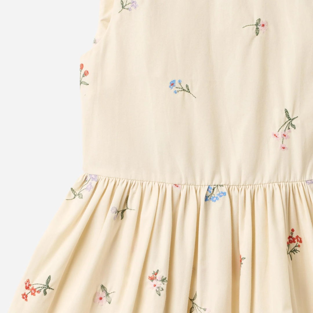 Sold at Bombon Shop, designed by Wheat, ivory organic cotton pinafore dress with embroidered floral details and gathered skirt.