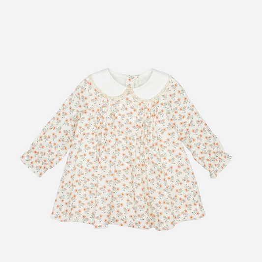 Sold at Bombon shop, designed by Fina Ejerique, a white viyella baby dress with pink and green floral print, Peter Pan collar with lace trim, pleated front, and long sleeves. front