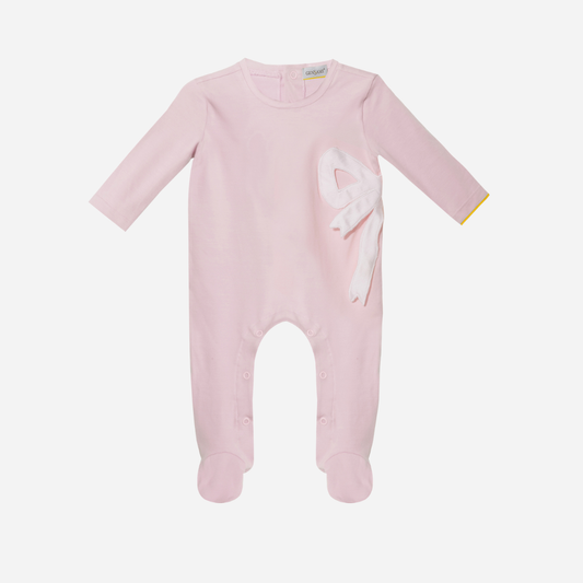 Sold at Bombon and designed by Gensami, a pale pink cotton baby romper with a white satin bow on the side and a yellow trim detail at the cuff.