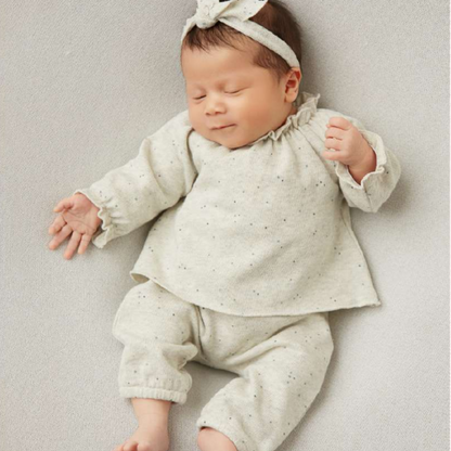 Sold at Bombon shop, designed by Tiny Soul — beige speckled knit baby blouse with gathered neckline and long puffed sleeves.model