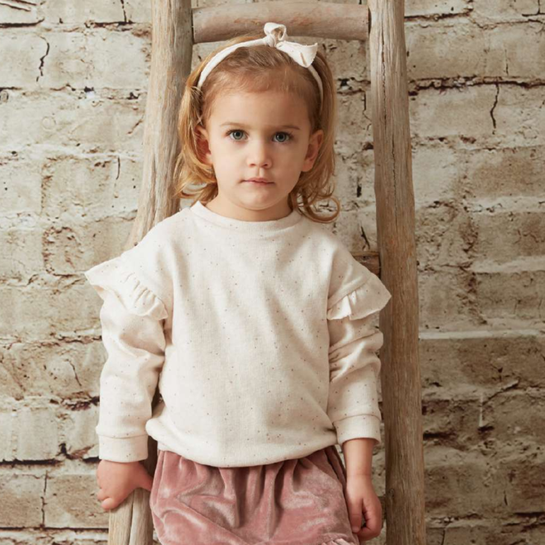 Sold at Bombon shop, designed by Tiny Soul — beige speckled baby sweatshirt with shoulder ruffles and long sleeves. model