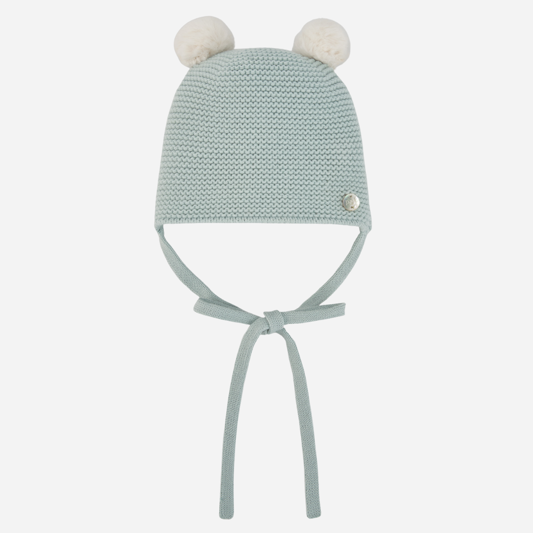 Sold at Bombon shop, designed by Paz Rodriguez, mint green baby knit beanie with two white pom-poms and chin ties.