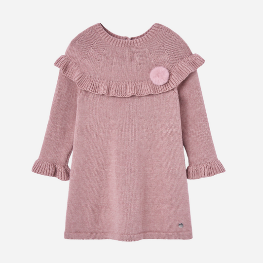 Sold at Bombon shop, designed by Paz Rodriguez. Pink knitted baby girl dress with ruffle trim, long sleeves, and pom-pom detail on the chest.