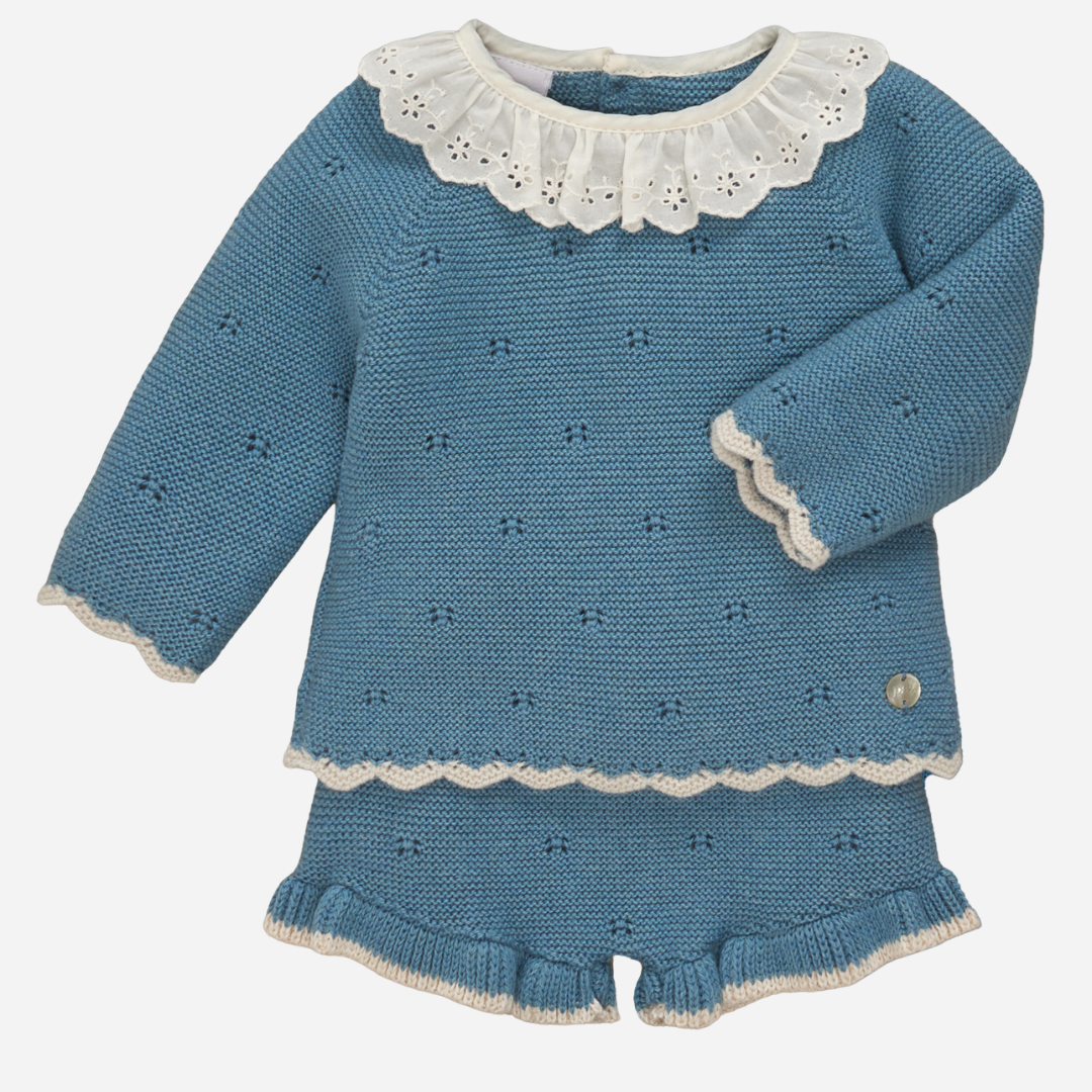 Sold at Bombon shop, designed by Paz Rodriguez, baby girl blue knit set with long-sleeve top, embroidered white collar, scalloped edges, and matching ruffle-trimmed shorts.