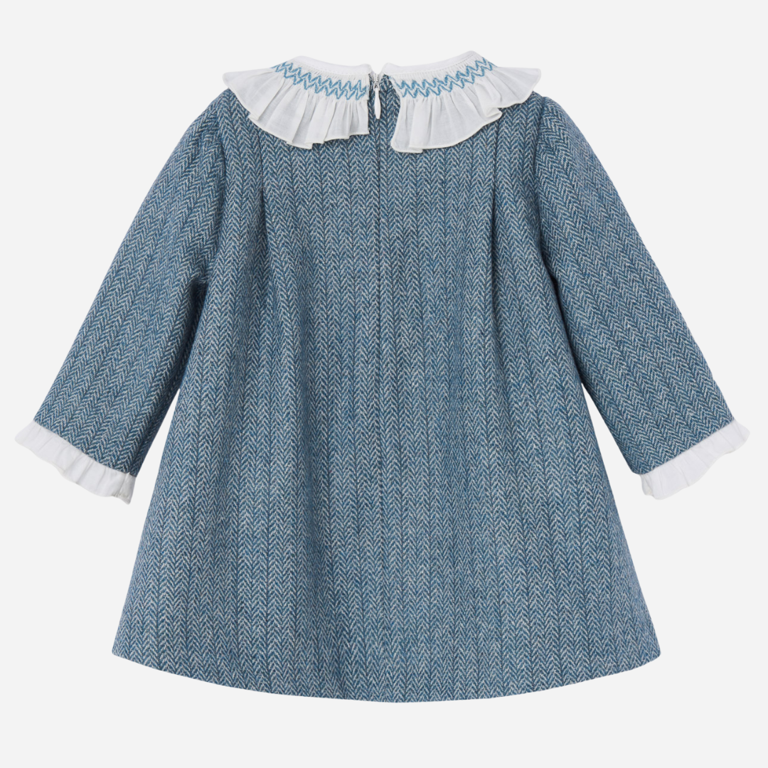 Sold at Bombon shop, designed by Paz Rodriguez. Blue herringbone baby girl dress with white ruffled collar, velvet bow, and long sleeves.