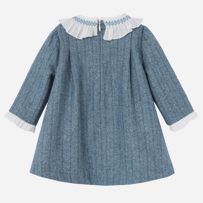 Sold at Bombon shop, designed by Paz Rodriguez. Blue herringbone baby girl dress with white ruffled collar, velvet bow, and long sleeves.