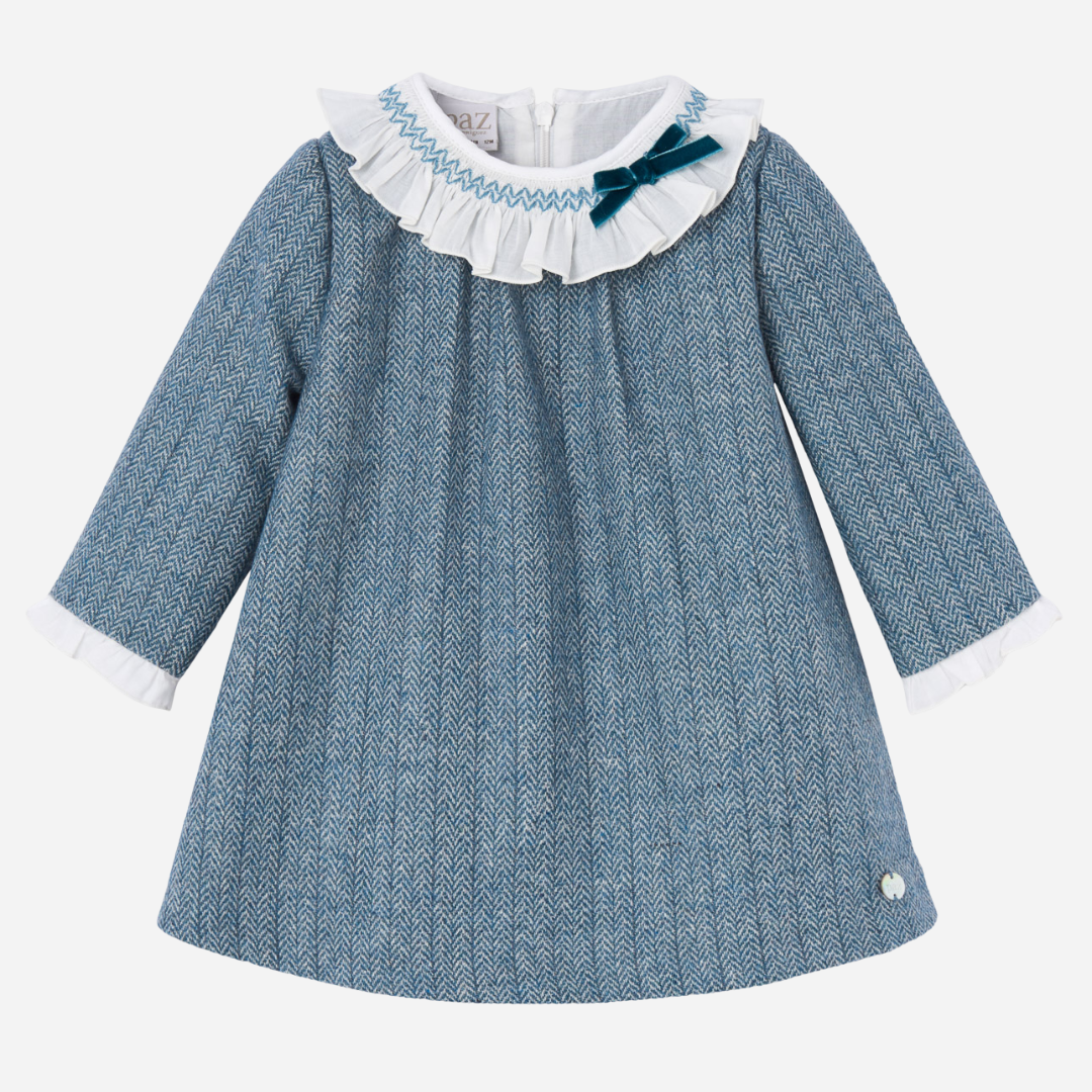 Sold at Bombon shop, designed by Paz Rodriguez. Blue herringbone baby girl dress with white ruffled collar, velvet bow, and long sleeves.