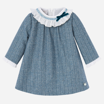 Sold at Bombon shop, designed by Paz Rodriguez. Blue herringbone baby girl dress with white ruffled collar, velvet bow, and long sleeves.