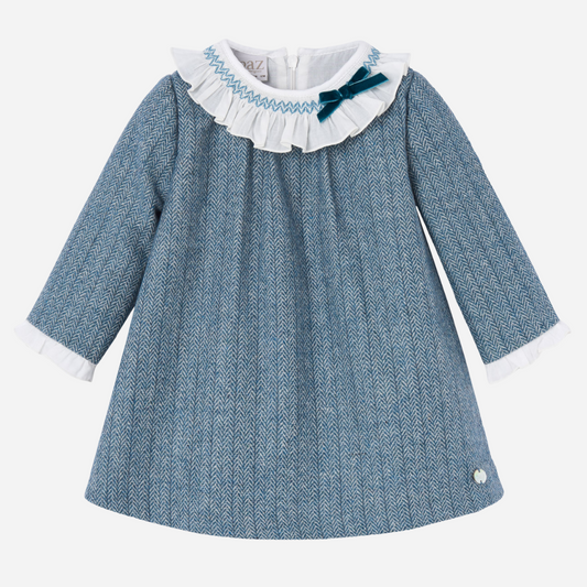 Sold at Bombon shop, designed by Paz Rodriguez. Blue herringbone baby girl dress with white ruffled collar, velvet bow, and long sleeves.