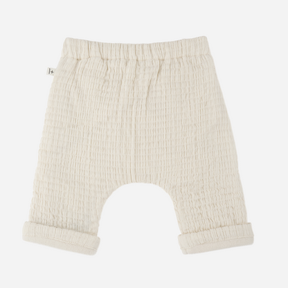 Sold at Bombon shop, designed by 1+ in the family — cream textured cotton muslin baby pants with rolled cuffs and adjustable drawstring waist. back