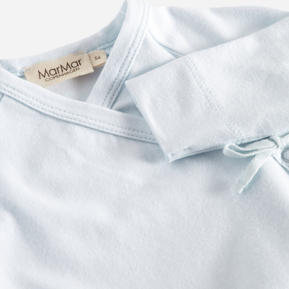 Sold at Bombon shop, designed by MarMar Copenhagen — powder blue organic cotton footed baby onesie with side tie closure.