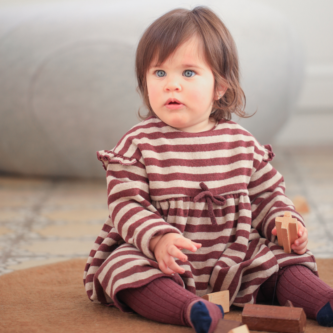 Sold at Bombon shop, designed by 1+ in the family — ribbed knit baby tights in melanzana with contrast navy toes and tan stripe detail. model