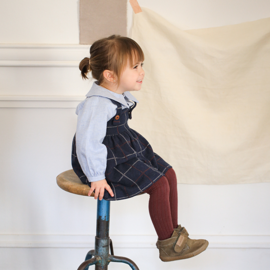 Sold at Bombon shop, designed by 1+ in the family — ribbed knit baby tights in melanzana with contrast navy toes and tan stripe detail. model