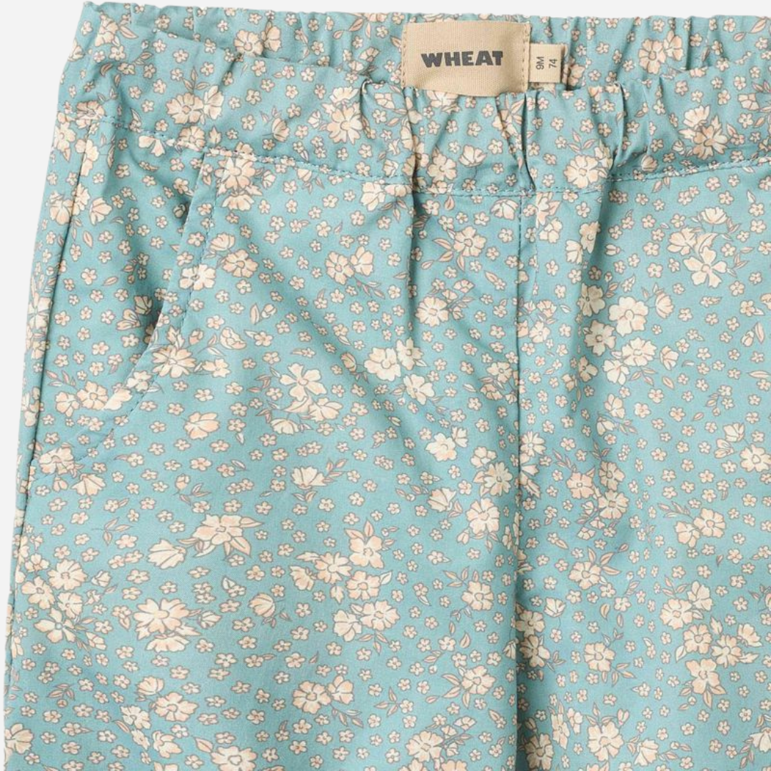 Sold at Bombon Shop, designed by Wheat, spring lake flowers organic cotton baby trousers in soft blue floral print with elastic waist and relaxed fit.