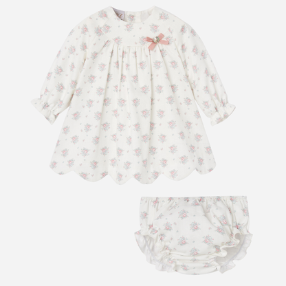 Sold at Bombon shop, designed by Paz Rodriguez, ivory baby dress with pink floral print, scalloped hem, pink bow detail, and matching bloomers.