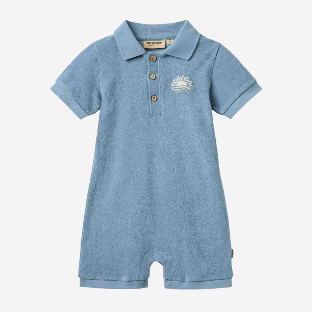 Sold at Bombon Shop, designed by Wheat, faded denim organic cotton short sleeve playsuit with polo collar and soft washed blue tone.