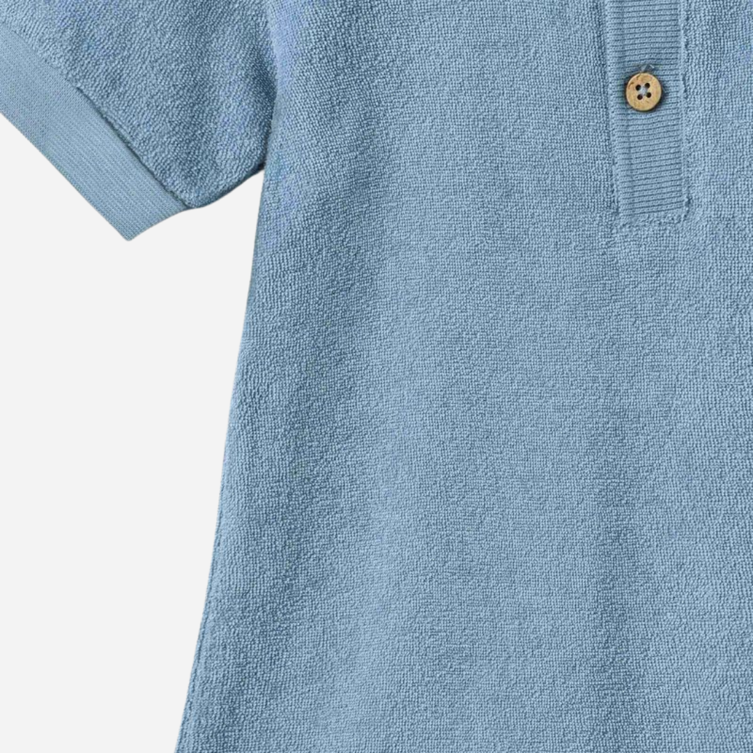 Sold at Bombon Shop, designed by Wheat, faded denim organic cotton short sleeve playsuit with polo collar and soft washed blue tone.