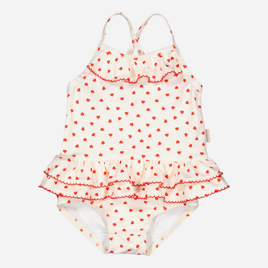 Sold at Bombon shop, designed by Mar Mar Copenhagen brand, this cute bathing suit in a small red heart print for baby girls and toddlers is perfect for spring and summer. front view