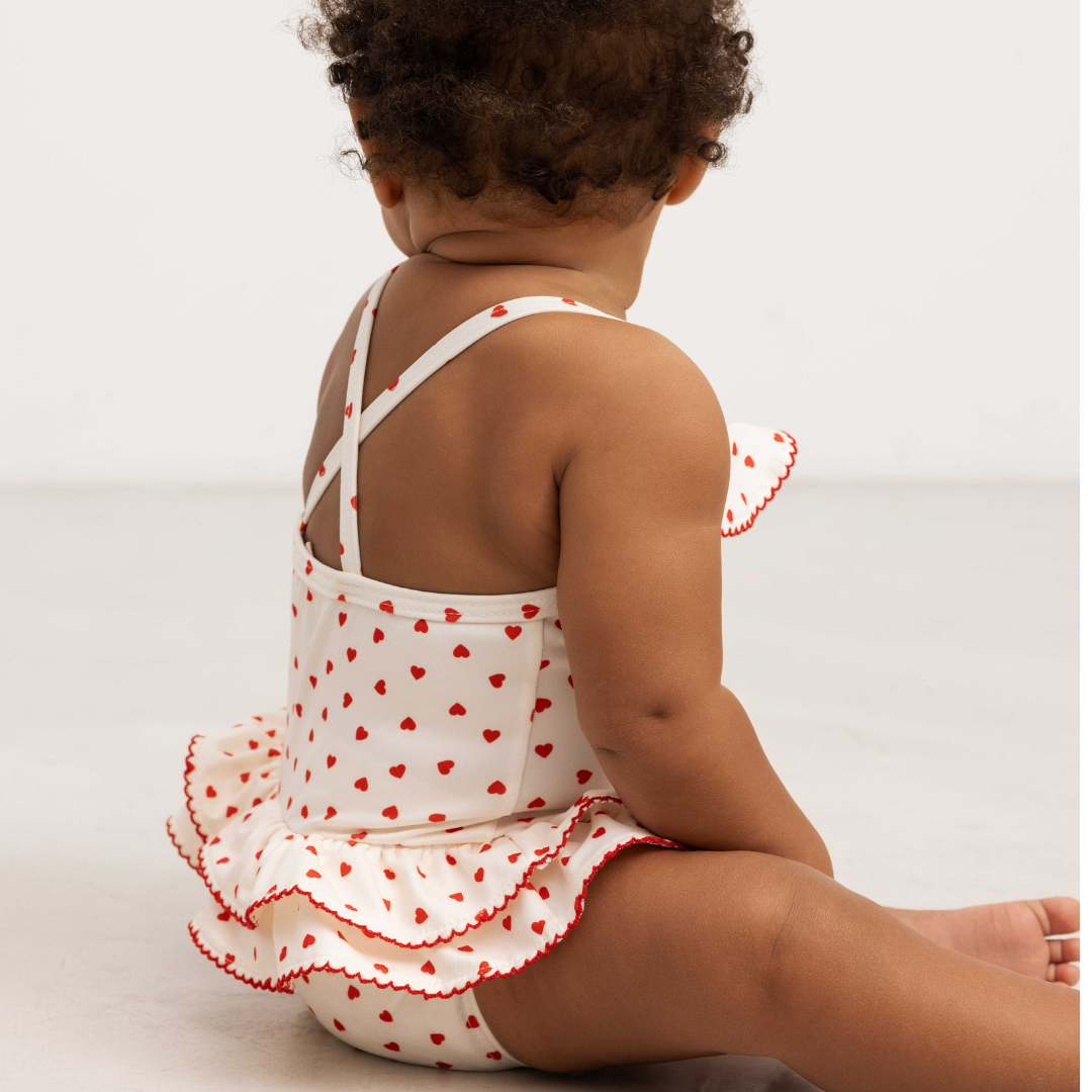 Sold at Bombon shop, designed by Mar Mar Copenhagen brand, this cute bathing suit in a small red heart print for baby girls and toddlers is perfect for spring and summer. model view back