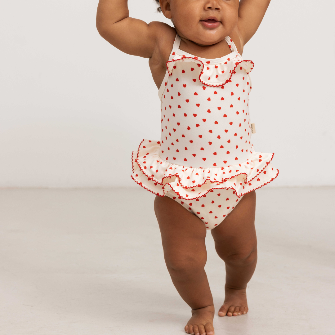Sold at Bombon shop, designed by Mar Mar Copenhagen brand, this cute bathing suit in a small red heart print for baby girls and toddlers is perfect for spring and summer. model view front