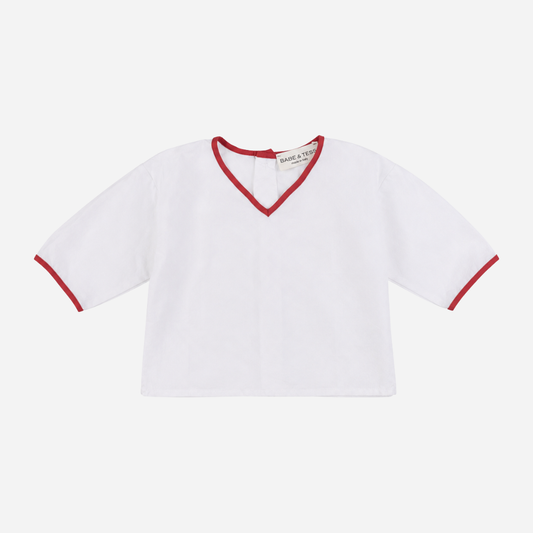 Sold at Bombon Shop, designed by Babe & Tess, white cotton top with a relaxed fit, V-neckline, short sleeves, and contrasting red trim details for a timeless summer look.